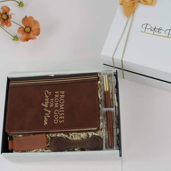 Close-up of a men’s gift box featuring a leather-like book, a wooden pen, a leather keychain, and cord organizers, perfect for gifting.