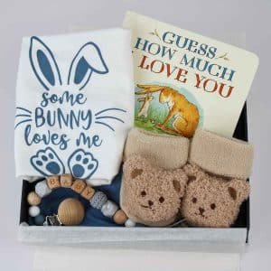 A beautifully arranged baby gift box containing a “Some Bunny Loves Me” onesie, teddy bear booties, a wooden pacifier clip, and the book “Guess How Much I Love You,” ideal for gifting.