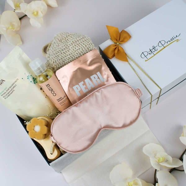 Contents of the spa gift box displayed outside the box, including bath salts, almond oil, a brightening face mask, a facial brush, a pink satin eye mask, and an exfoliating mitt, ideal for gifting.