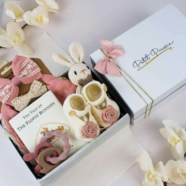Baby girl gift box with pink ribbon, Petit Pressie branding, book, crocheted bunny, shoes, and teether