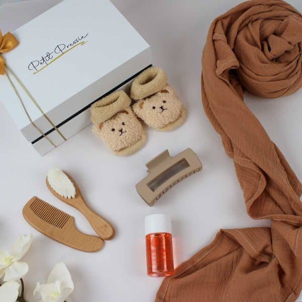 Neutral baby gift set with teddy socks, grooming tools, and brown wrap next to Petit Pressie box