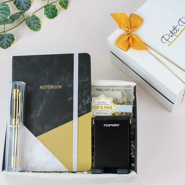 Black and gold office gift set with notebook, gold pen, phone stand, and clips in a white gift box