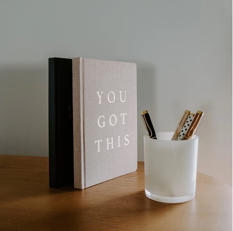 You Got This Gift Box - Motivational Essentials Set 6 Beige “YOU GOT THIS” journal standing next to a black notebook and a white cup holding elegant pens