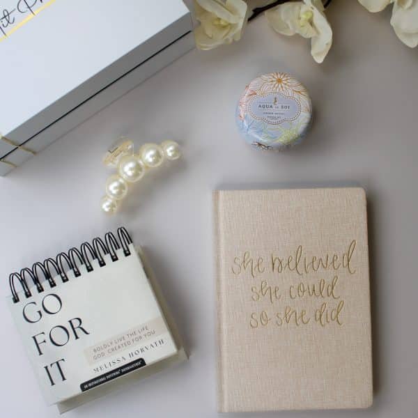 Flat lay of a Christian gift set with journal, calendar, candle, and pearl clip