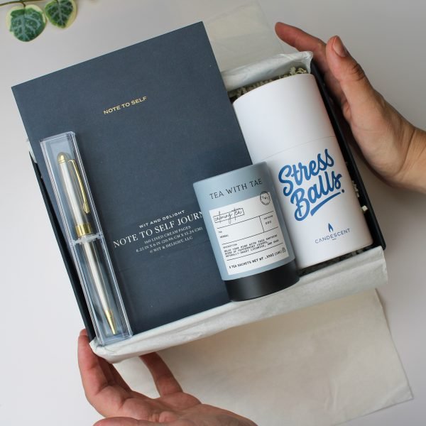 Hands holding a wellness gift box with calming tea, stress relief candle, journal, and pen – Petit Pressie encouragement set